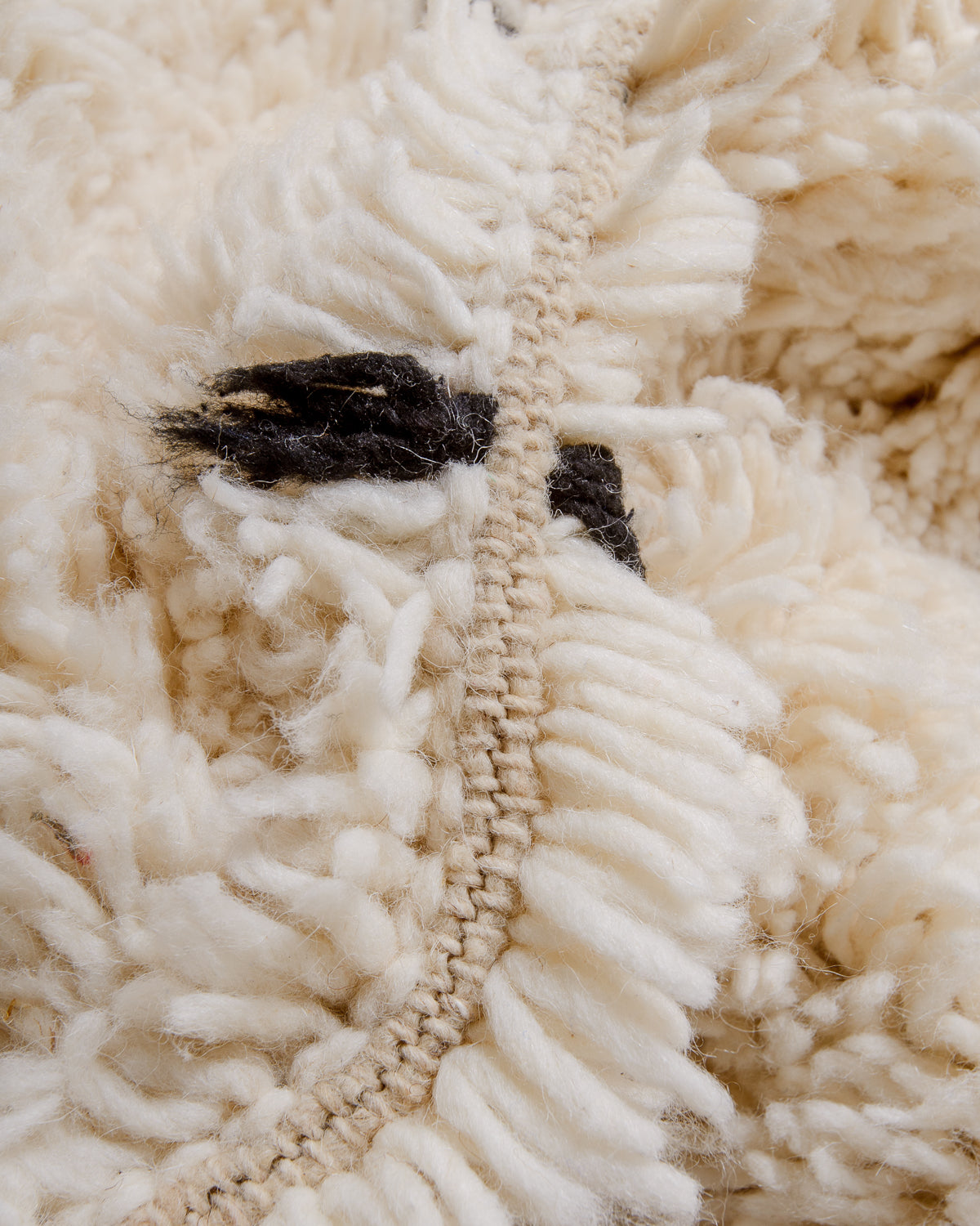 Detail of cream wool rug showing the density of the wool and black strands that make up the polka dots.